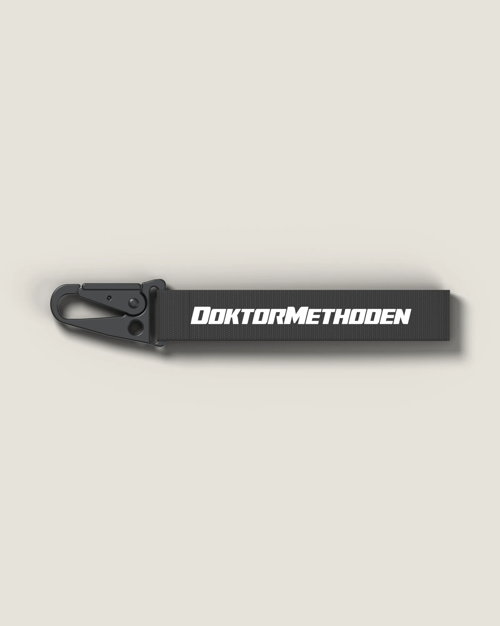 Schwarzer Karabiner Strap, quer liegend, mit DOKTORMETHODEN-Schriftzug und Karabiner links